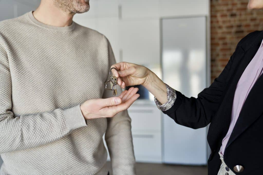 Pessoa entregando um chaveiro com chaves em formato de casa para outra, simbolizando a compra ou aluguel de imóvel.